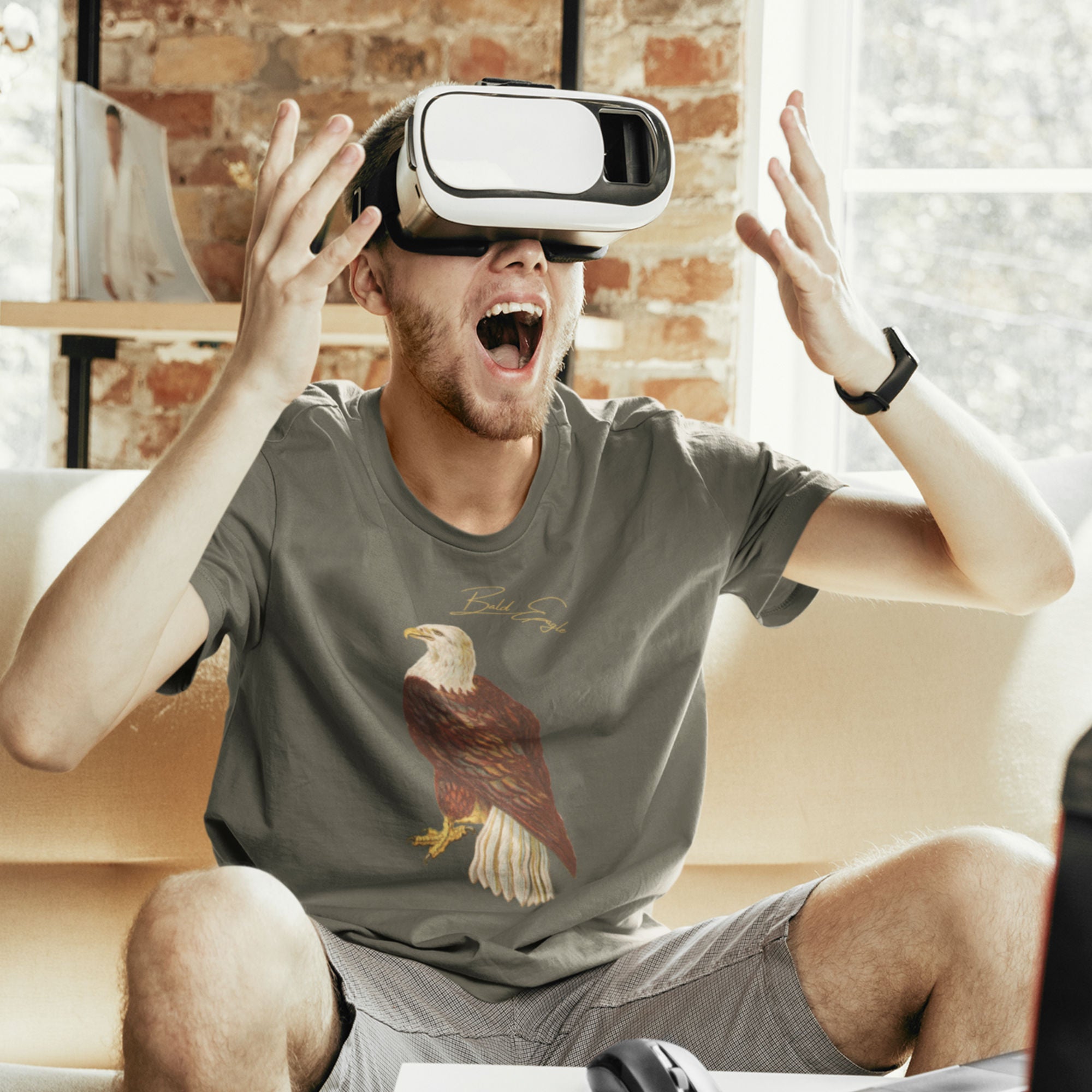 Army green bird shirt with vintage artwork of a bald eagle and the words "Bald Eagle" centered above the art. Worn by a man wearing virtual reality goggles and viewing what can only be assumed to be a bird.