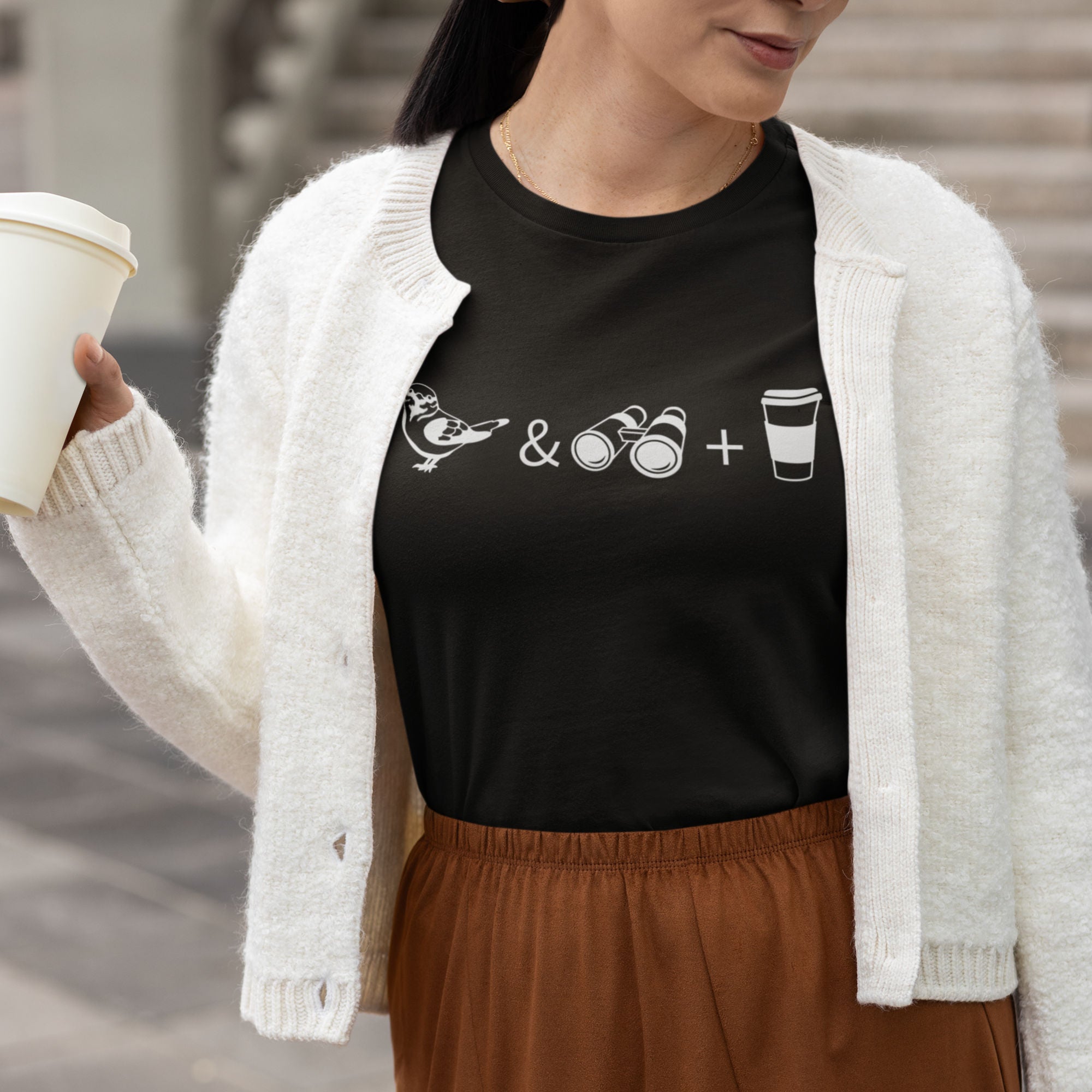 Black women's bird t-shirt celebrating bird watching and coffee with a graphic of binoculars, a bird, and a travel cup of coffee. Worn by a woman.