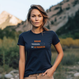 Navy blue bird shirt with the words Birding in Progress on the front around a loading progress bar, worn by a woman on the beach.