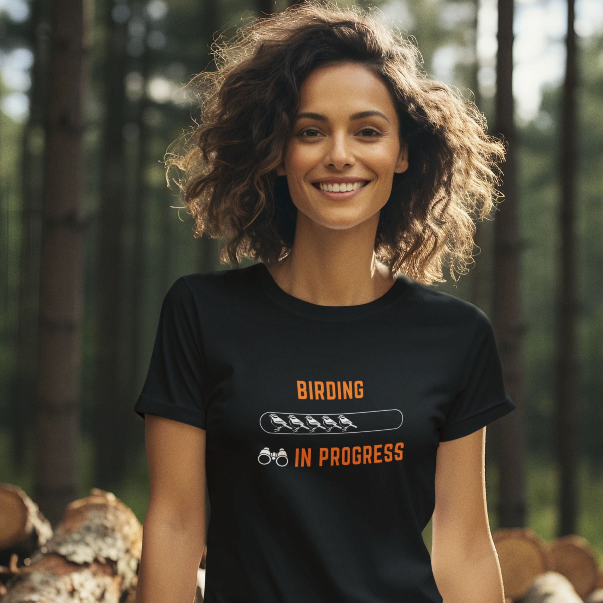 Black bird shirt with the words Birding in Progress on the front around a loading progress bar. Worn by a woman in the woods.