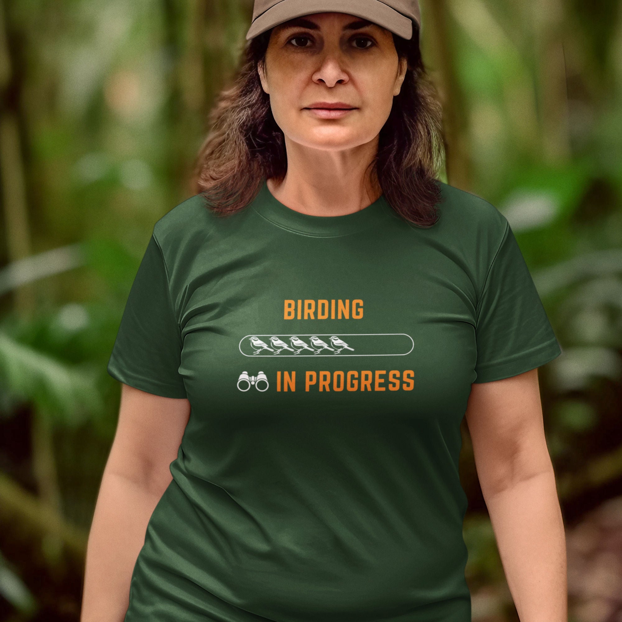 Forest green bird shirt with the words Birding in Progress on the front around a loading progress bar. Worn by a woman in the woods.