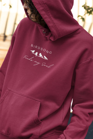 Maroon hoodie with the words Birdsong feeds my should above and below a white graphic of 4 birds on a branch. Worn by a woman.