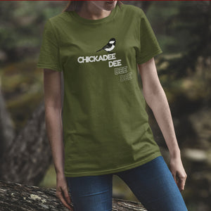 Olive birder shirt with a Chickadee and the words Chickadee dee dee dee on the front. Worn by a woman in the woods.