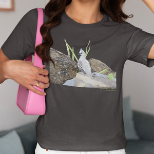 Dark gray unisex bird t-shirt with a graphic of a crested pigeon among some rocks and grass on front, and the words crested pigeon written below and the scientific name below that. Worn by a woman.