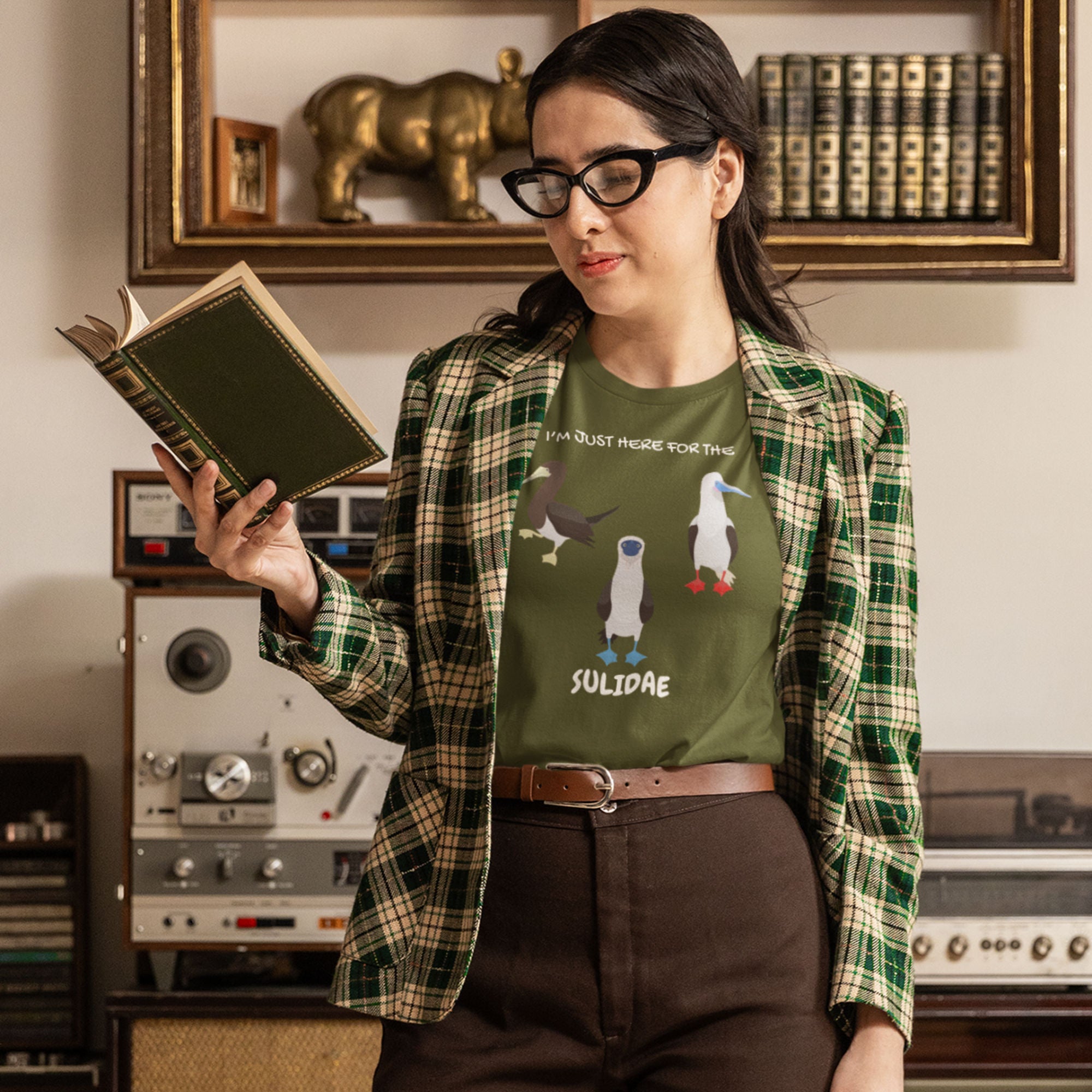 Olive green birder shirt with a red-footed, blue-footed and brown booby on it, but referencing only the scientific family name for the bird. Worn by a woman.