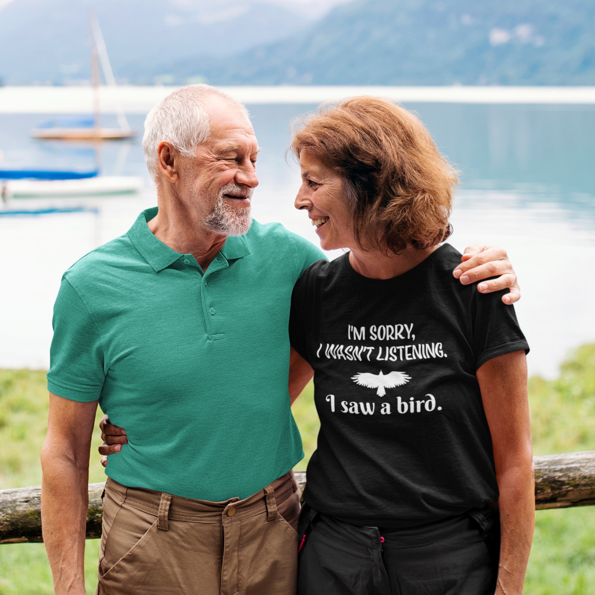 Black bird t-shirt with the words I'm sorry I wasn't listening, I saw a bird. And a graphic of a bird flying. Worn by a woman standing by a fence with her husband.