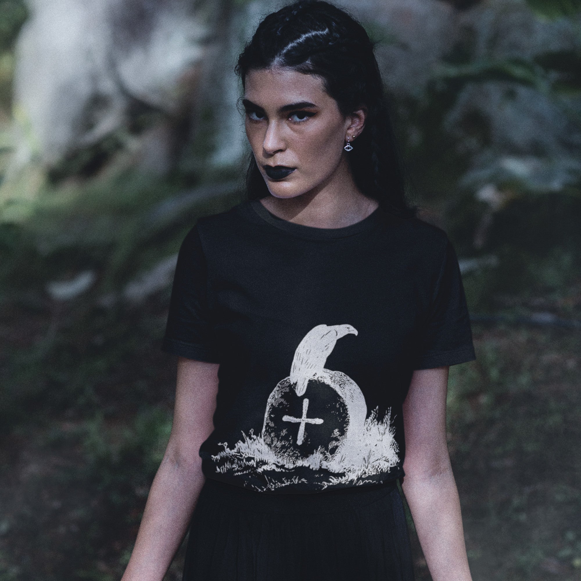 Black bird t-shirt with a picture of raven sitting on top of an unmarked grave. Worn by a gothic almost wiccan looking woman in the woods.