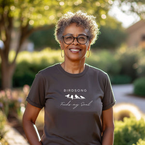 Gray t-shirt with the words Birdsong feeds my soul placed above and below a white graphic of 4 birds on a branch. Worn by a woman.