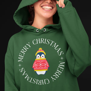 Forest green unisex bird hoodie with Merry Christmas on the front in a circle that surrounds a cute penguin in a hat and a sweater. Worn by a smiling person.