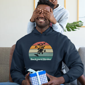 Navy blue bird hoodie with a retro sun design outlining a bird feeder with the words Backyard Birder. Worn by a man sitting on a couch.