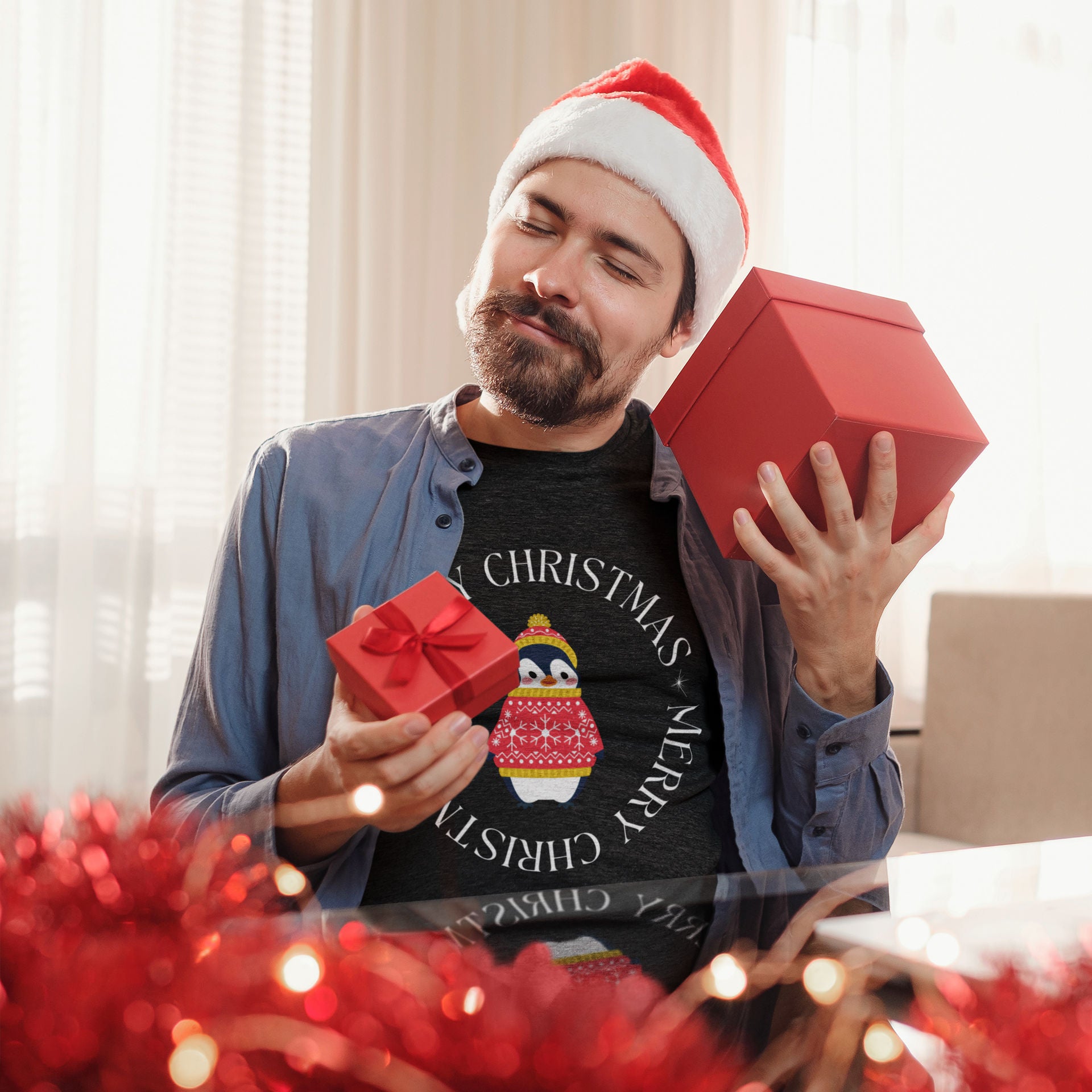 Dark heather grey unisex bird t-shirt with Merry Christmas on the front in a circle that surrounds a cute penguin in a hat and a sweater. Worn by a man opening gifts.