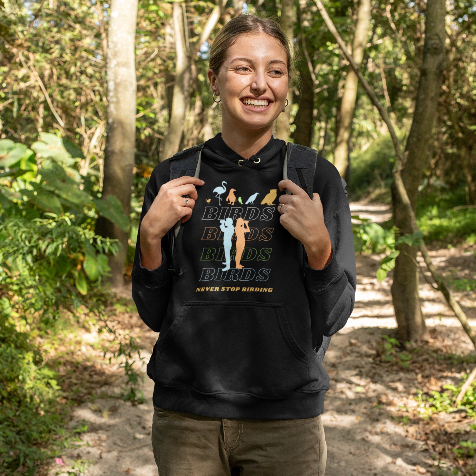 Black unisex birding hoodie that has silhouettes of a man and a woman using binoculars overlayed on a stack of the word Birds with the saying, "Never Stop Birding" at the bottom and colorful silhouette of different birds at the top.