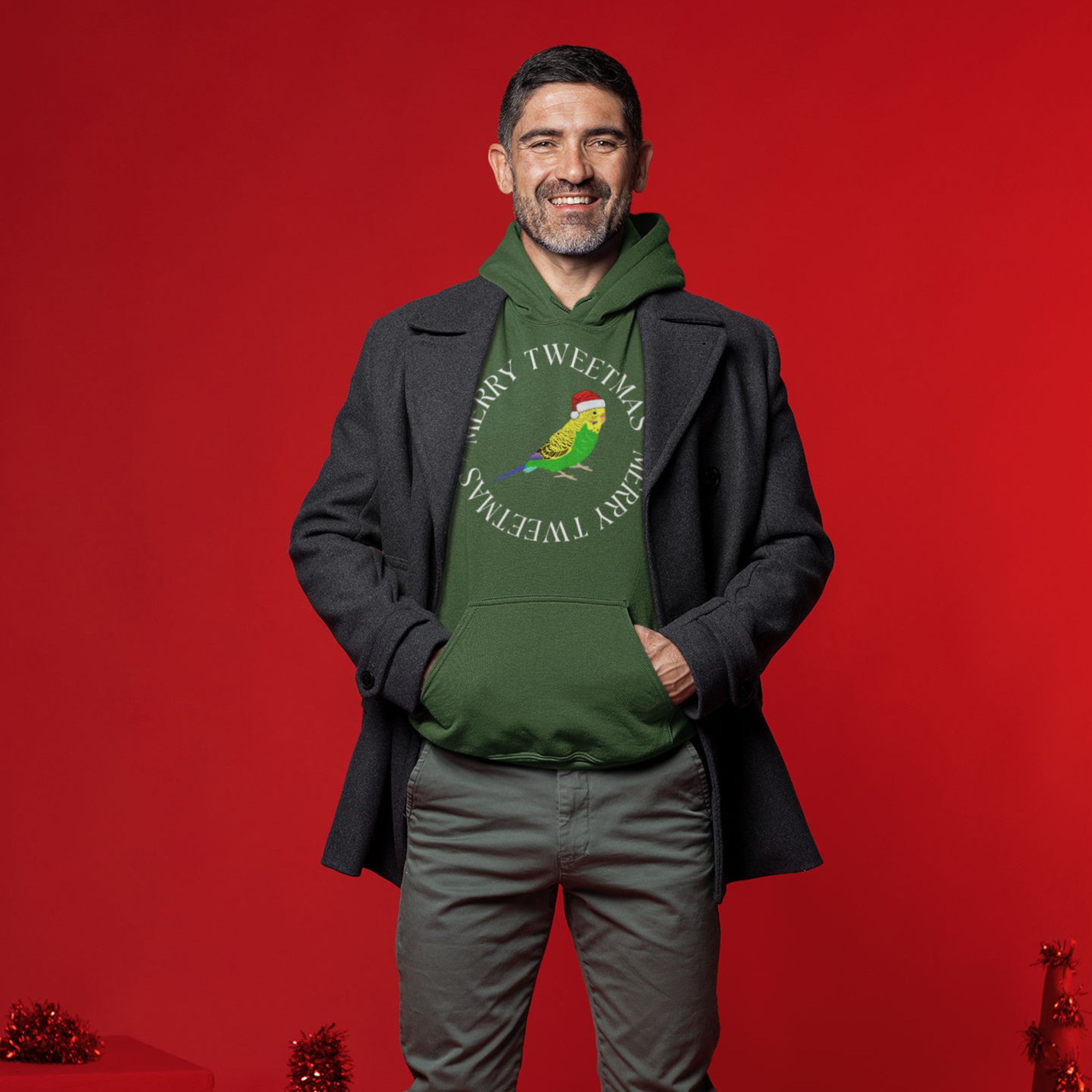 Forest geen unisex bird hoodie with a budgie in a santa hat surrounded by the words Merry Tweetmas, separated by to seed sprigs. Worn by a happy man.