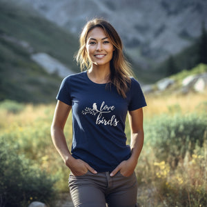 Navy blue unisex birding t-shirt with the words Love birds and a graphic of a bird on a branch in white. Worn by a woman in nature.