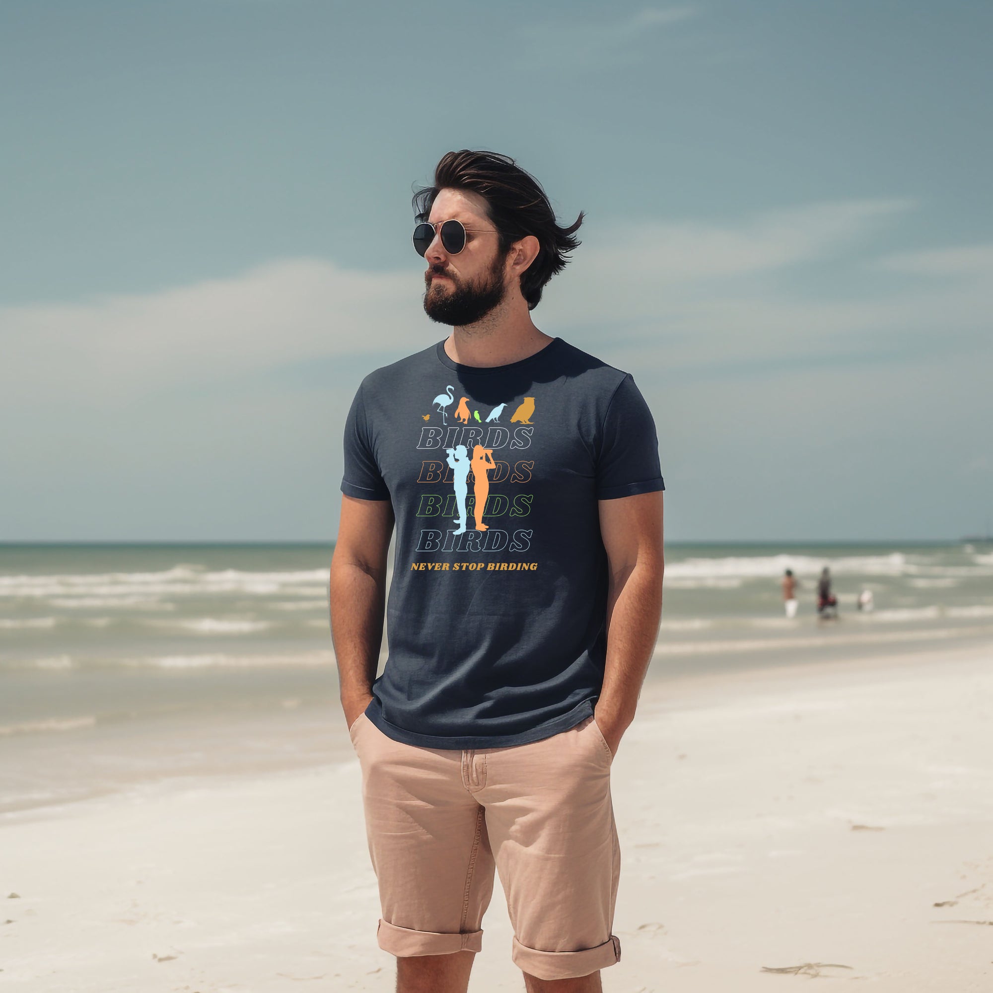 Navy blue unisex birding t-shirt that has silhouettes of a man and a woman using binoculars overlayed on a stack of the word Birds with the saying, "Never Stop Birding" at the bottom and colorful silhouette of different birds at the top. Worn by a man.