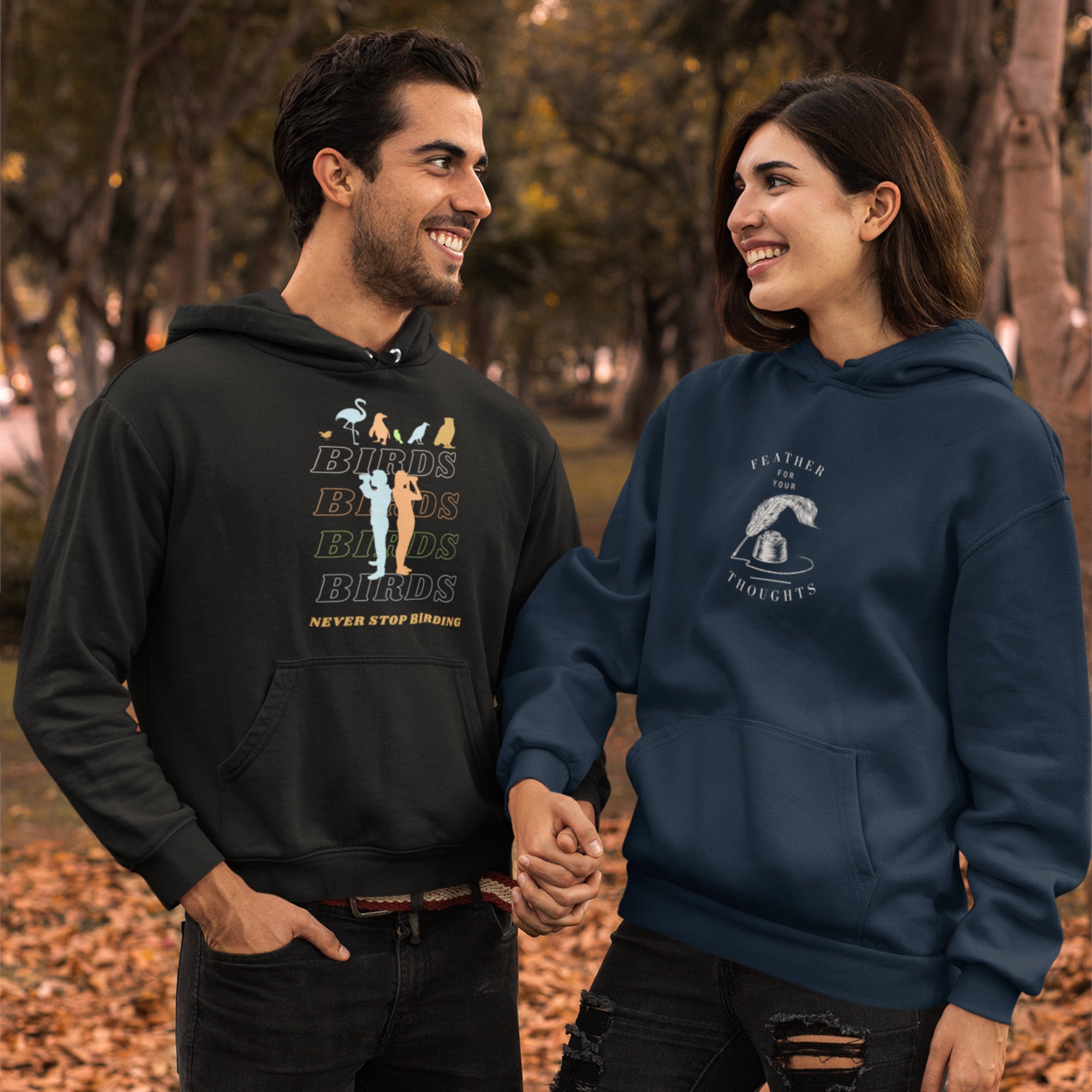 Black unisex birding hoodie that has silhouettes of a man and a woman using binoculars overlayed on a stack of the word Birds with the saying, "Never Stop Birding" at the bottom and colorful silhouette of different birds at the top. Worn by a man holding the hand of a woman wearing another awesome hoodie.