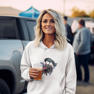 White unisex bird hoodie with a crow holding a heart pendant, perched upon a skull, surrounded by wings and flowers. Worn by a woman at a tailgate party.