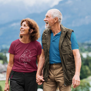 Maroon unisex bird shirt featuring a line drawing of two Albatross heads and the words "For Life" on the front. Worn by a woman walking in nature with her husband.