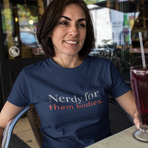 Navy Blue unisex bird shirt with the words Nerdy for them birdies on the front in two coordinating fonts and colors. Worn by a woman having a drink at an outdoor cafe.