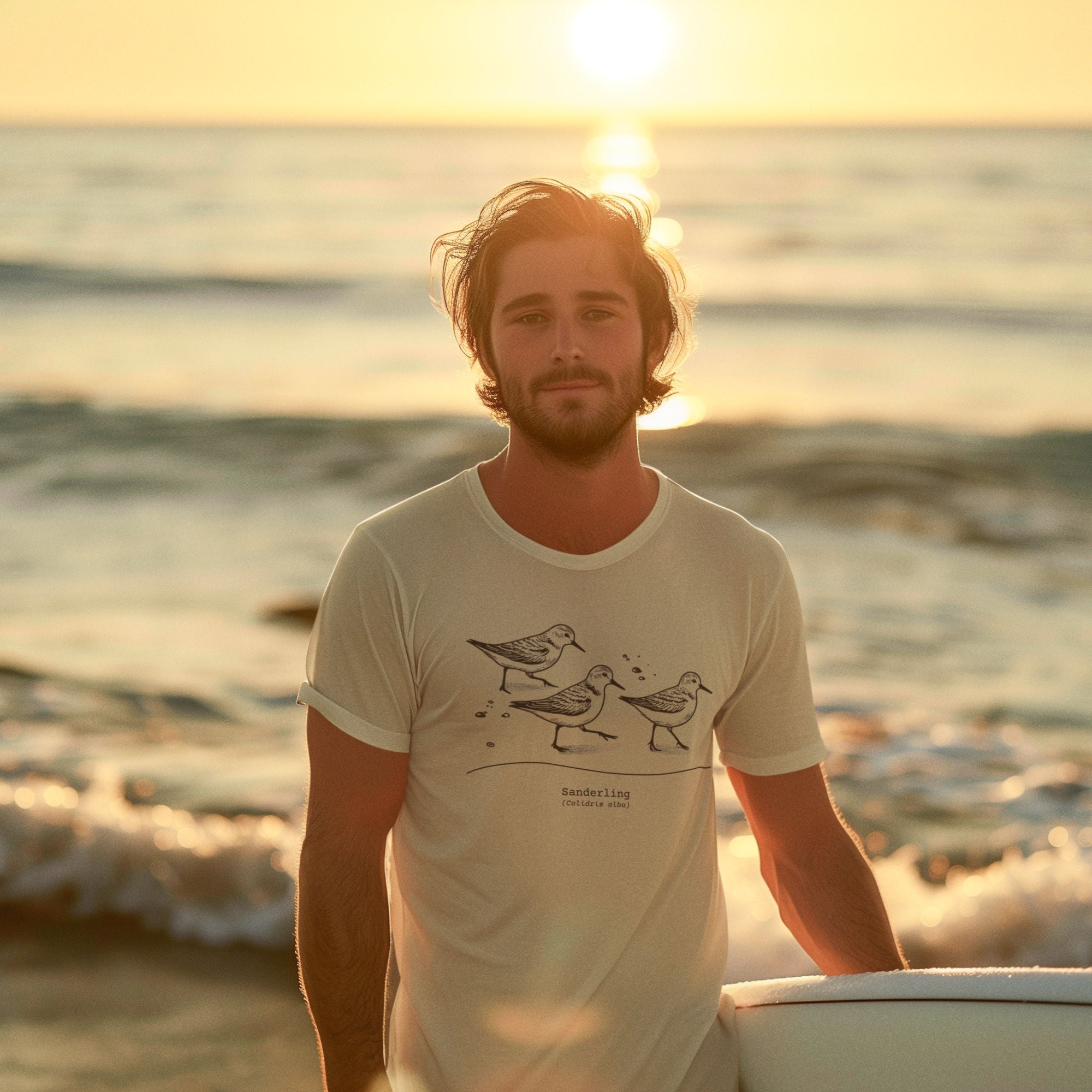 Cream colored bird shirt featuring an illustration of a three sanderlings on a beach and the common and scientific names for the bird underneath. Worn by a man on a beach.