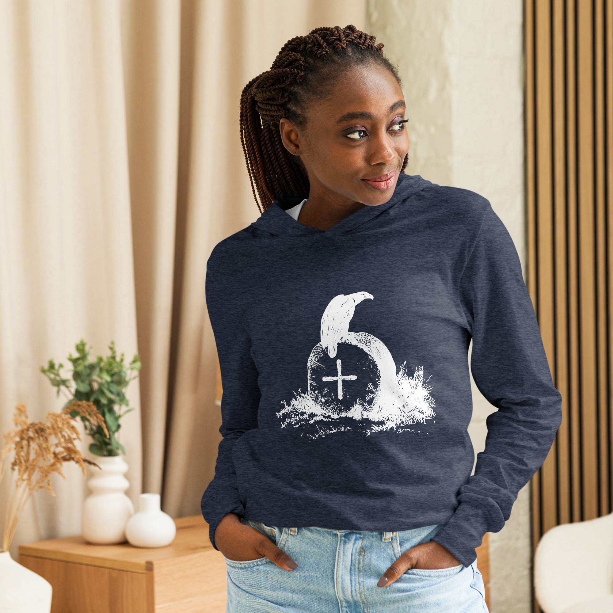 Navy heather, long-sleeve, hooded bird t-shirt with a raven perches on a grave. Spooky. Worn by a woman.