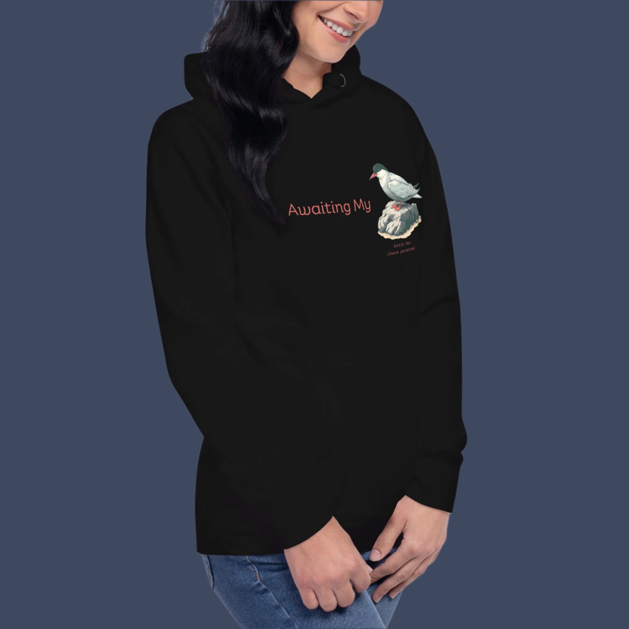 Black unisex hoodie with a graphic of an Arctic Tern on a rock, and the words "Awaiting My" next to it in a fun pun. The words Arctic Tern and the scientific name of Sterna Paradisaea are below the bird. Worn by a woman.