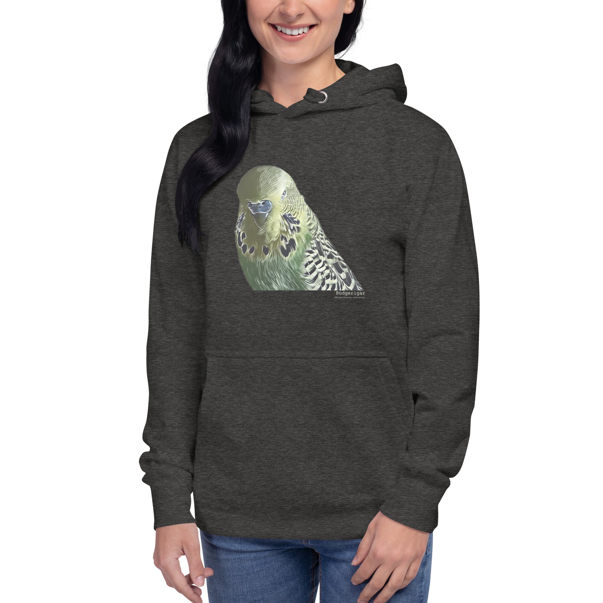 Dark heather gray unisex bird hoodie with an illustrated and lifelike graphic of a green and yellow parakeet or budgie on the front. Below and to the right of the picture is the word Budgerigar and below that the scientific name in parenthesis in small print. Worn by a woman.