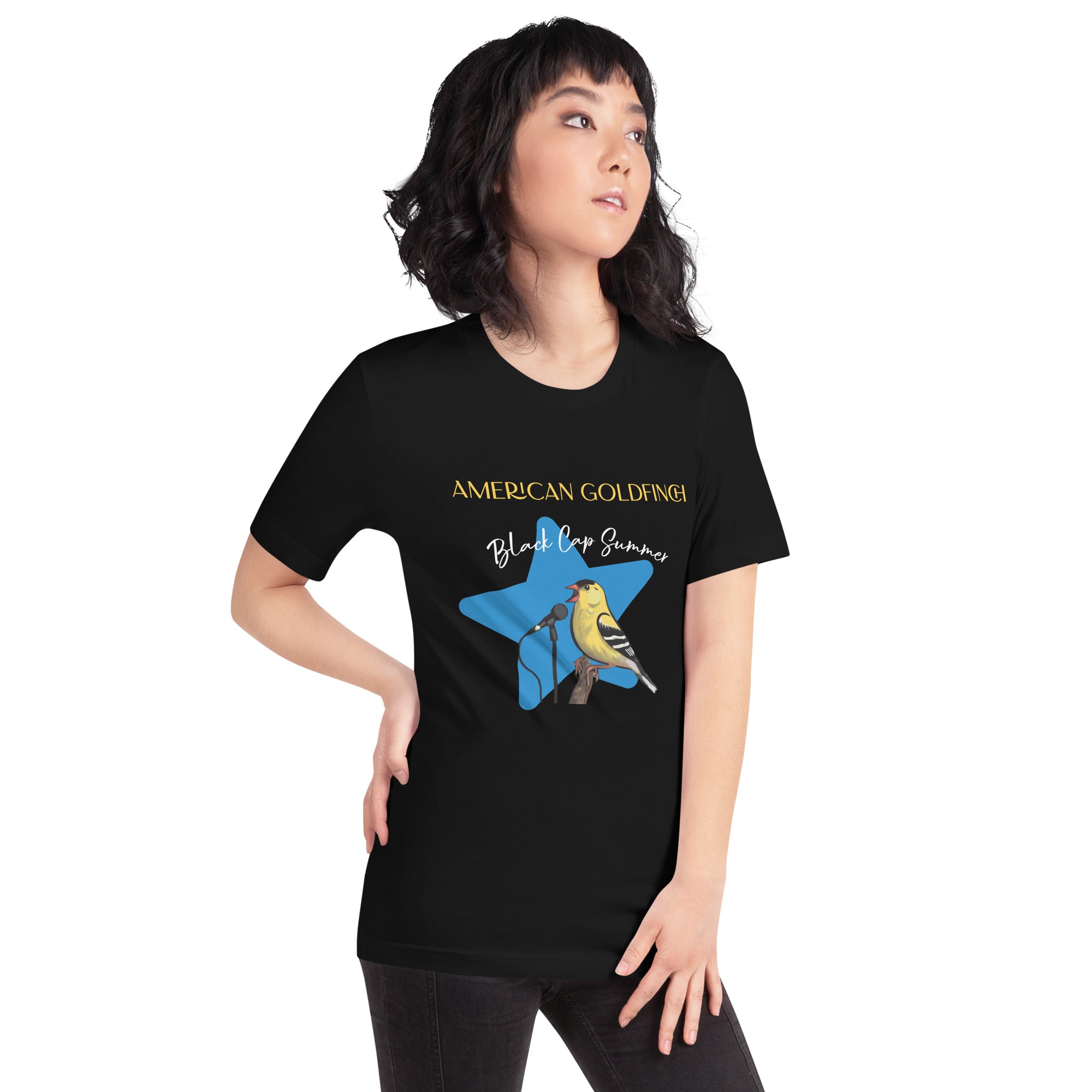 Black unisex bird shirt featuring an American goldfinch singing into a microphone with a list of dates and cities on the back where the bird is commonly seen. Worn by a woman.