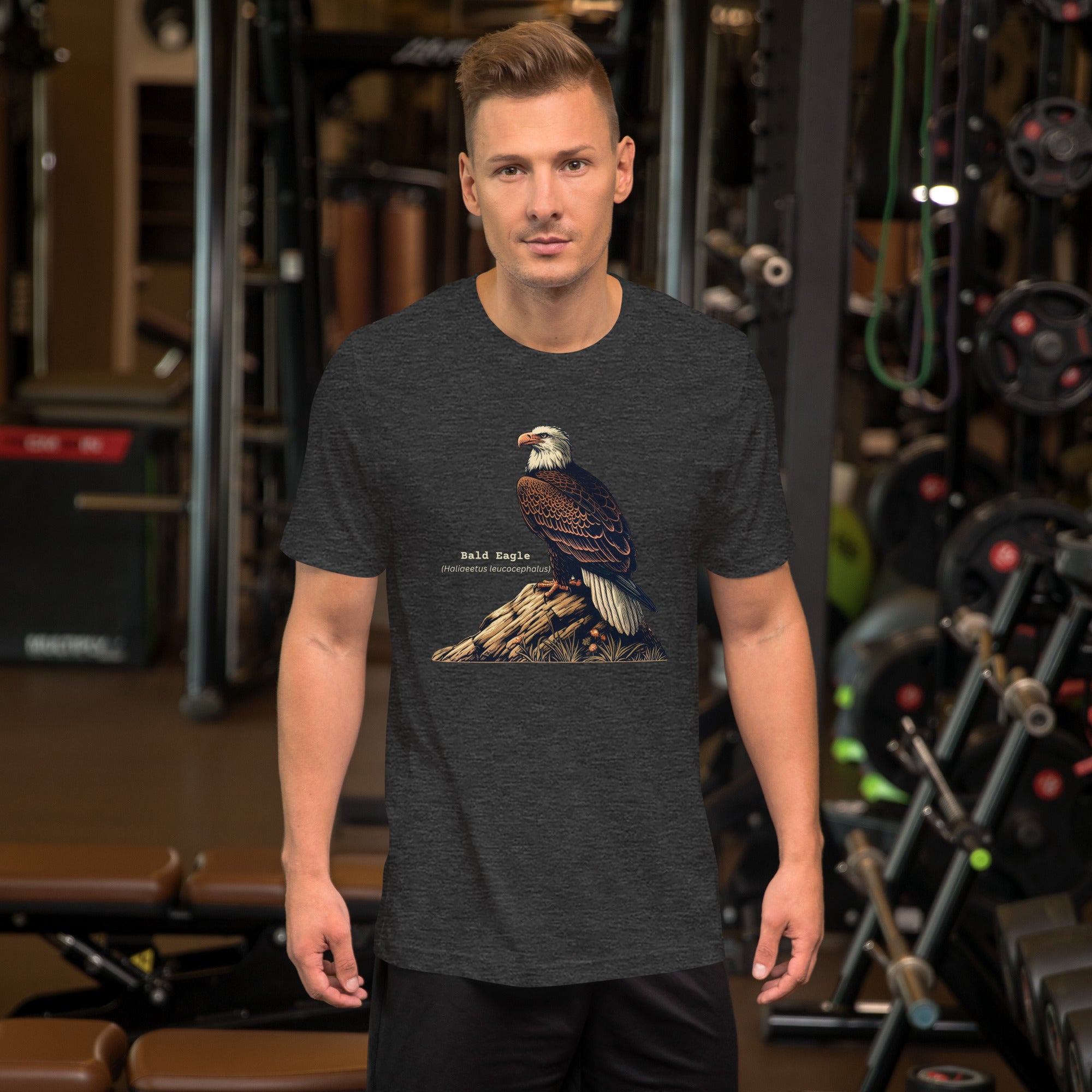 Dark heather gray bird shirt with an artistic depiction of aBald Eagle sitting on a rock and the birds common and scientific names next to the bird. Worn by a man at the gym.