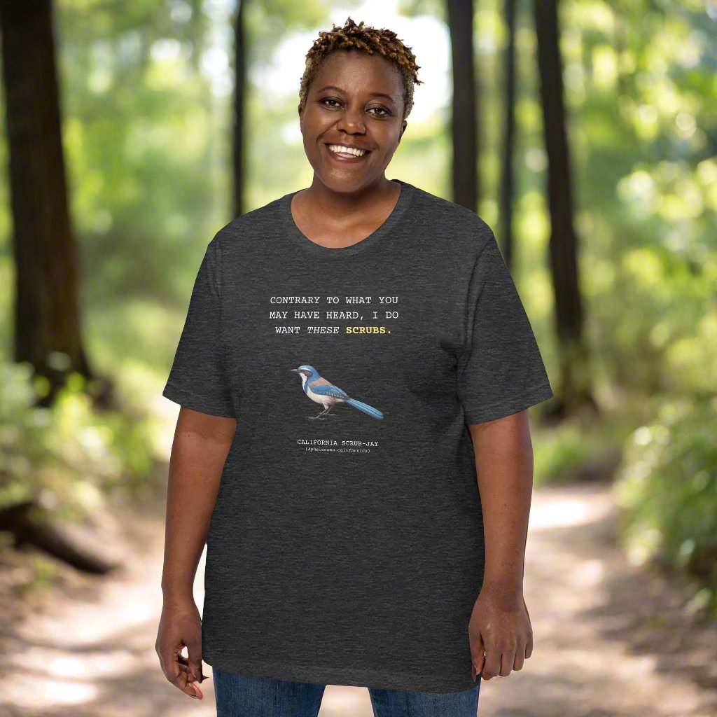 A dark Heather gray unisex bird shirt with the words I want these scrubs on the front above an illustration of a California scrub-jay. Worn by a woman.