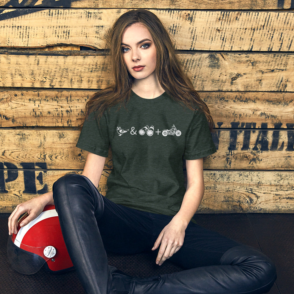 Unisex forest green bird t-shirt celebrating bird watching and motorcycling with a graphic of binoculars, a bird, and a motorcycle. Worn by a woman with sitting next to a scooter helmet.