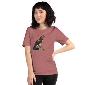 Mauve bird shirt with an artistic depiction of a red-tailed hawk sitting on a fence and the common and scientific names for the bird next to it. Worn by a woman.