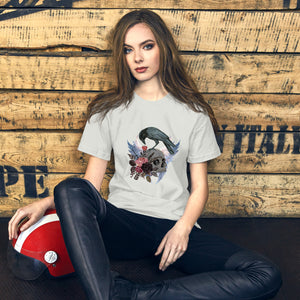 Gothic themed silver bird shirt with a crow carrying a heart pendant, perched on a skull surrounded by flowers, feathers and wings. Worn by a woman.