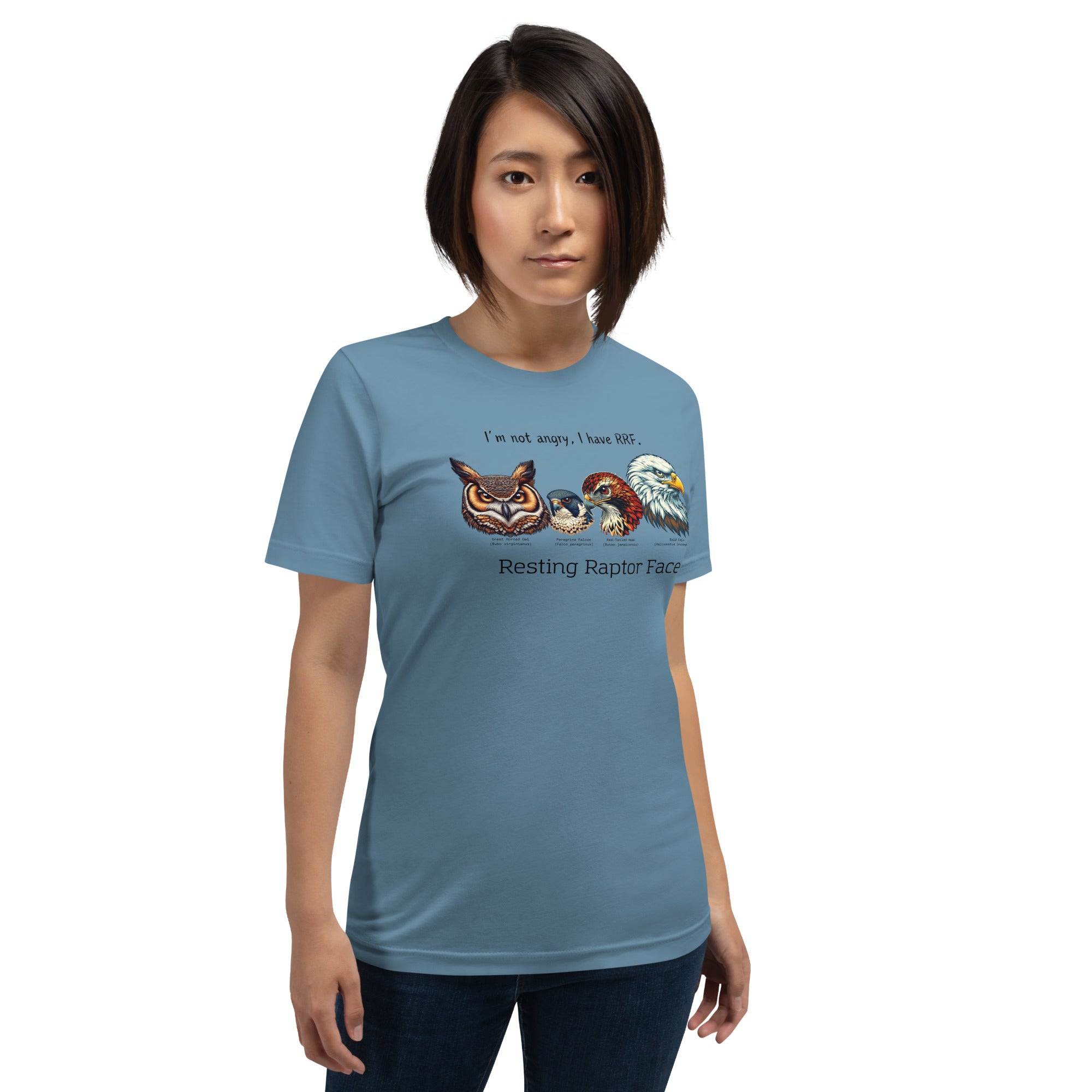 Woman wearing a steel blue bird shirt with a great horned owl, a peregrine falcon, a red-tailed hawk and a bald eagle. The shirt has text that says, I'm not angry, I have RRF. Resting Raptor Face.