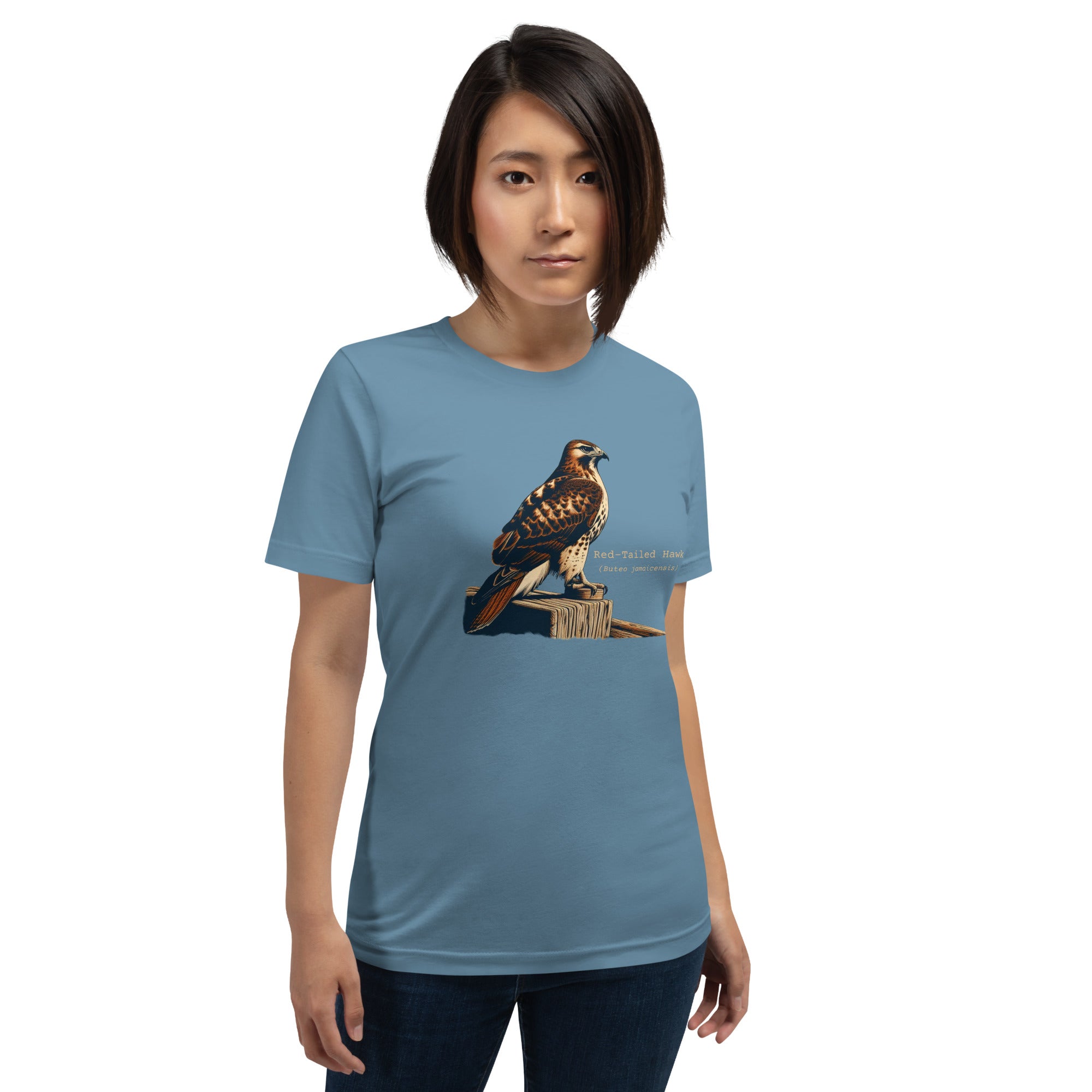 Steel blue bird shirt with an artistic depiction of a red-tailed hawk sitting on a fence and the common and scientific names for the bird next to it. Worn by a woman.