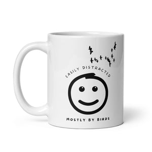 White 11oz mug with the words "Easily distracted, mostly by Birds" surrounding a smiley face with eyes looking up toward a flock of birds.