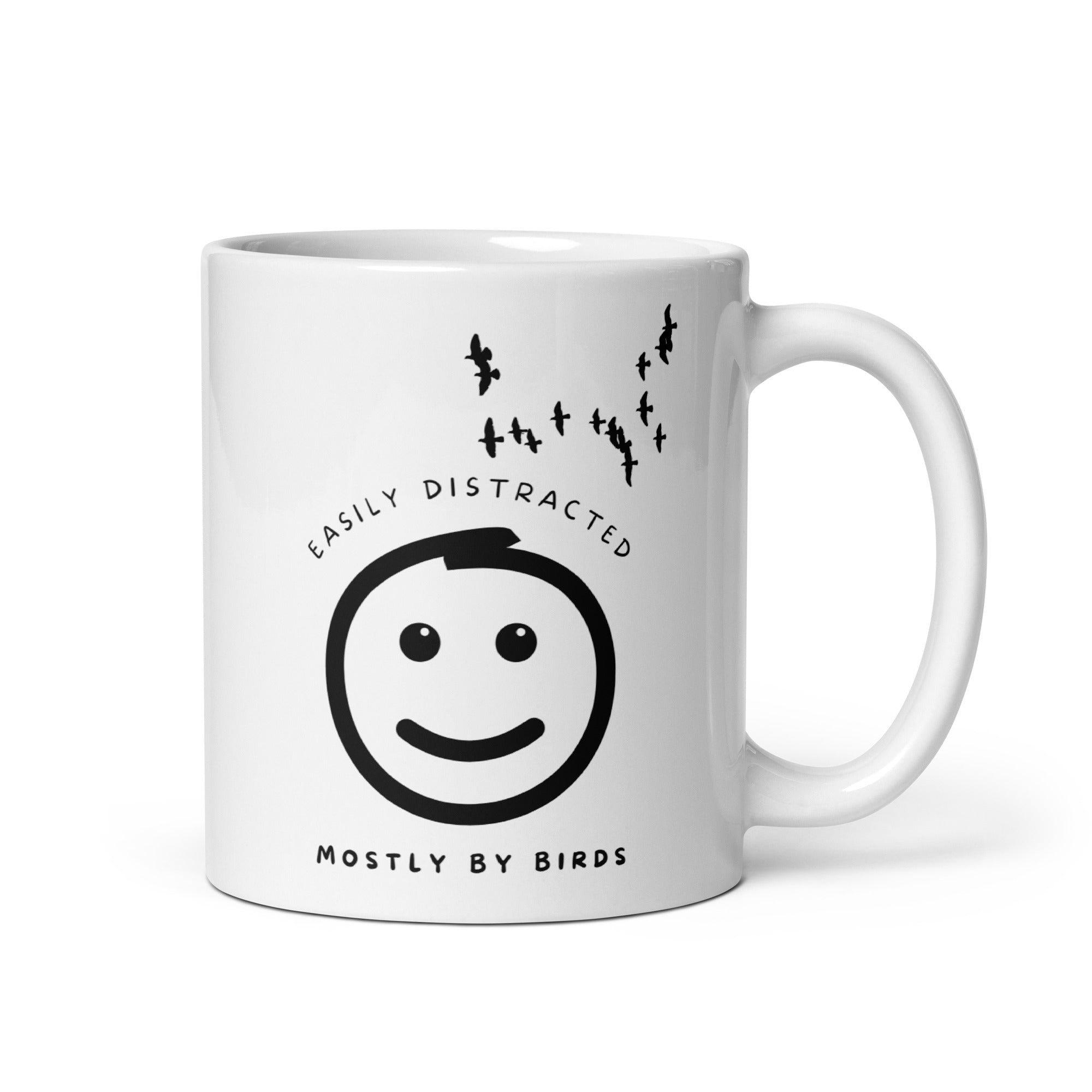 White 11oz mug with the words "Easily distracted, mostly by Birds" surrounding a smiley face with eyes looking up toward a flock of birds.