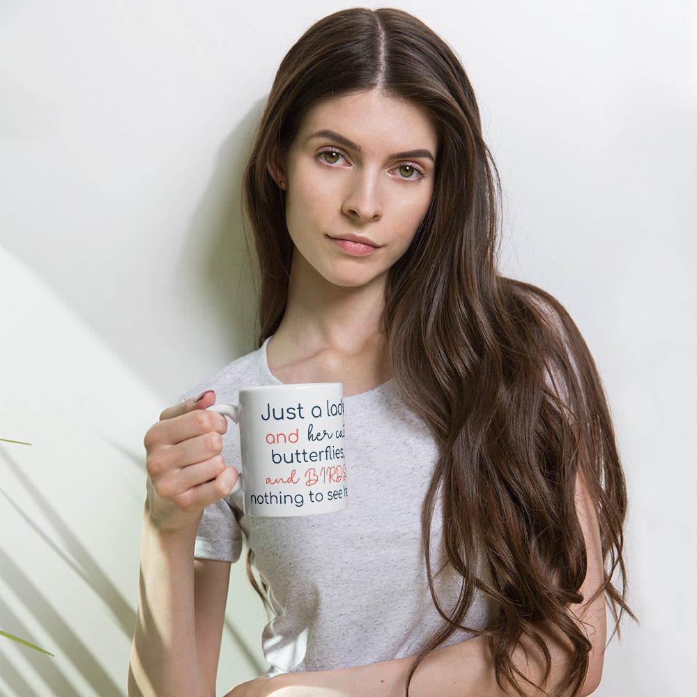 Coffee mug with a remaster version of Lady and her Pets on one side and the words, "Just a lady and her cat, butterflies, and Birds..., nothing to see here." on the the other side.