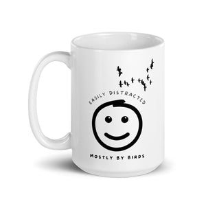 White 15oz mug with the words "Easily distracted, mostly by Birds" surrounding a smiley face with eyes looking up toward a flock of birds.