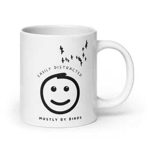 White 20oz mug with the words "Easily distracted, mostly by Birds" surrounding a smiley face with eyes looking up toward a flock of birds.