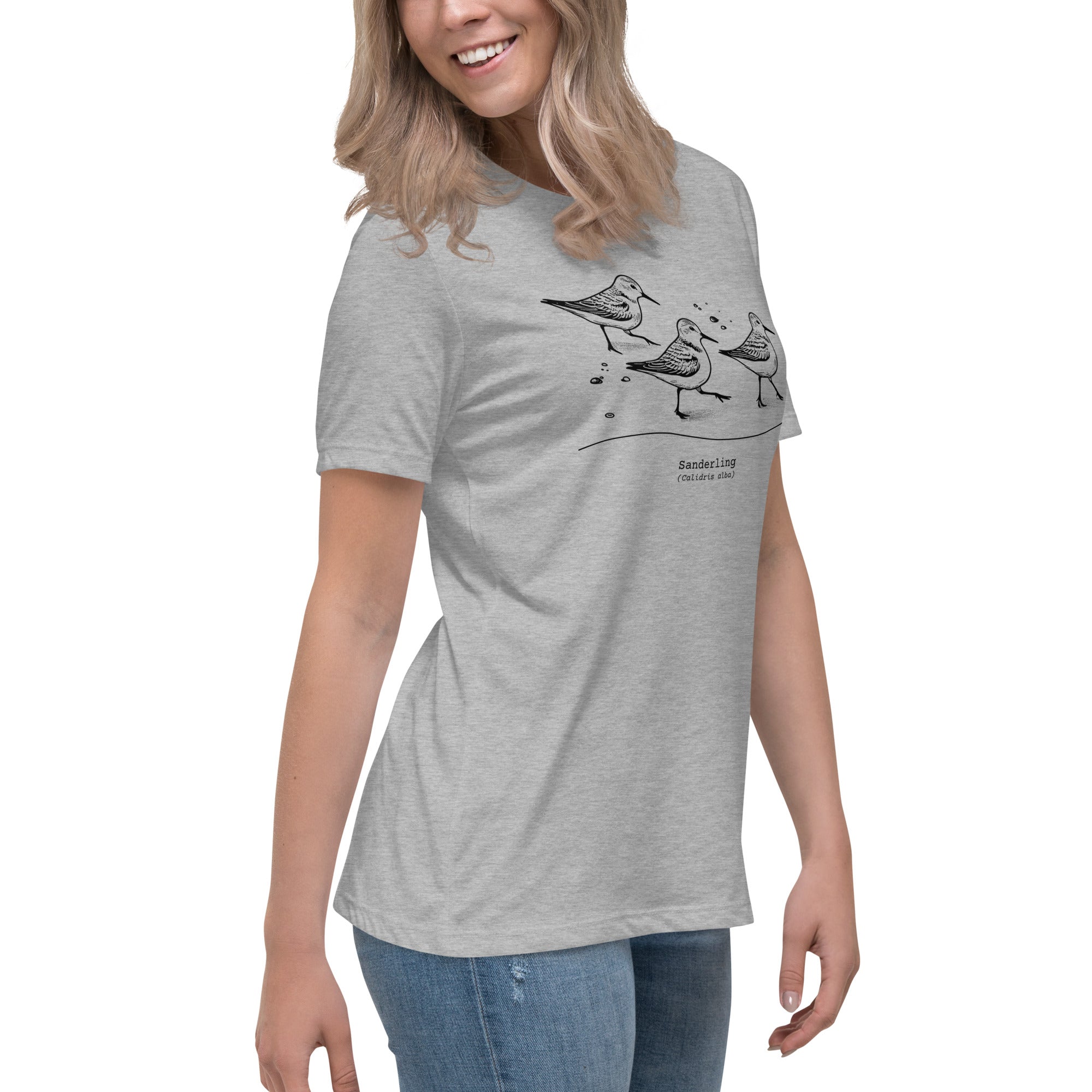 Light heather gray bird shirt featuring an illustration of a three sanderlings on a beach and the common and scientific names for the bird underneath. Worn by a woman.