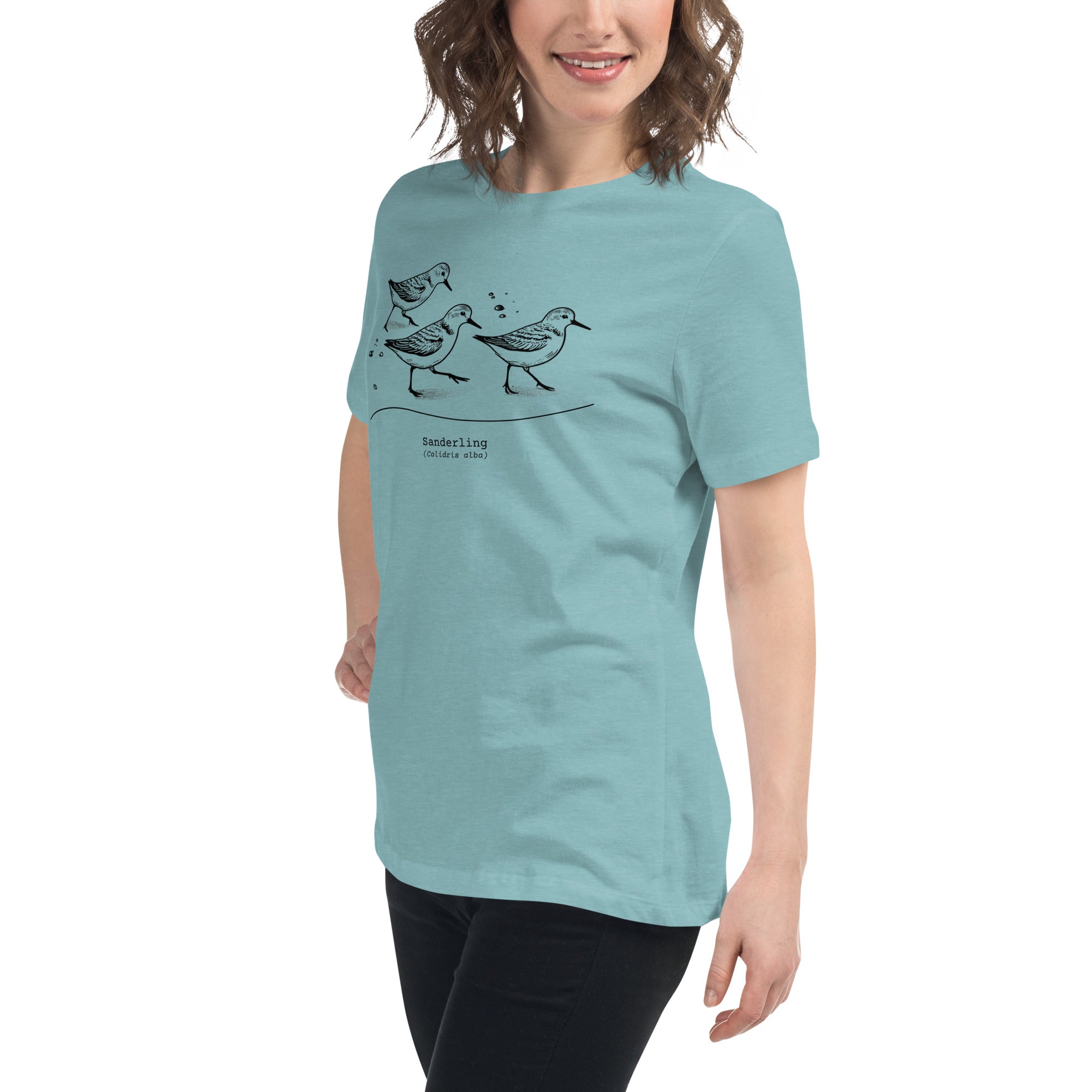 Light heather blue bird shirt featuring an illustration of a three sanderlings on a beach and the common and scientific names for the bird underneath. Worn by a woman.