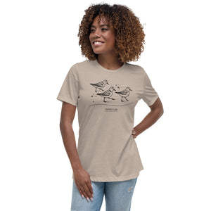 Light heather tan bird shirt featuring an illustration of a three sanderlings on a beach and the common and scientific names for the bird underneath. Worn by a woman.