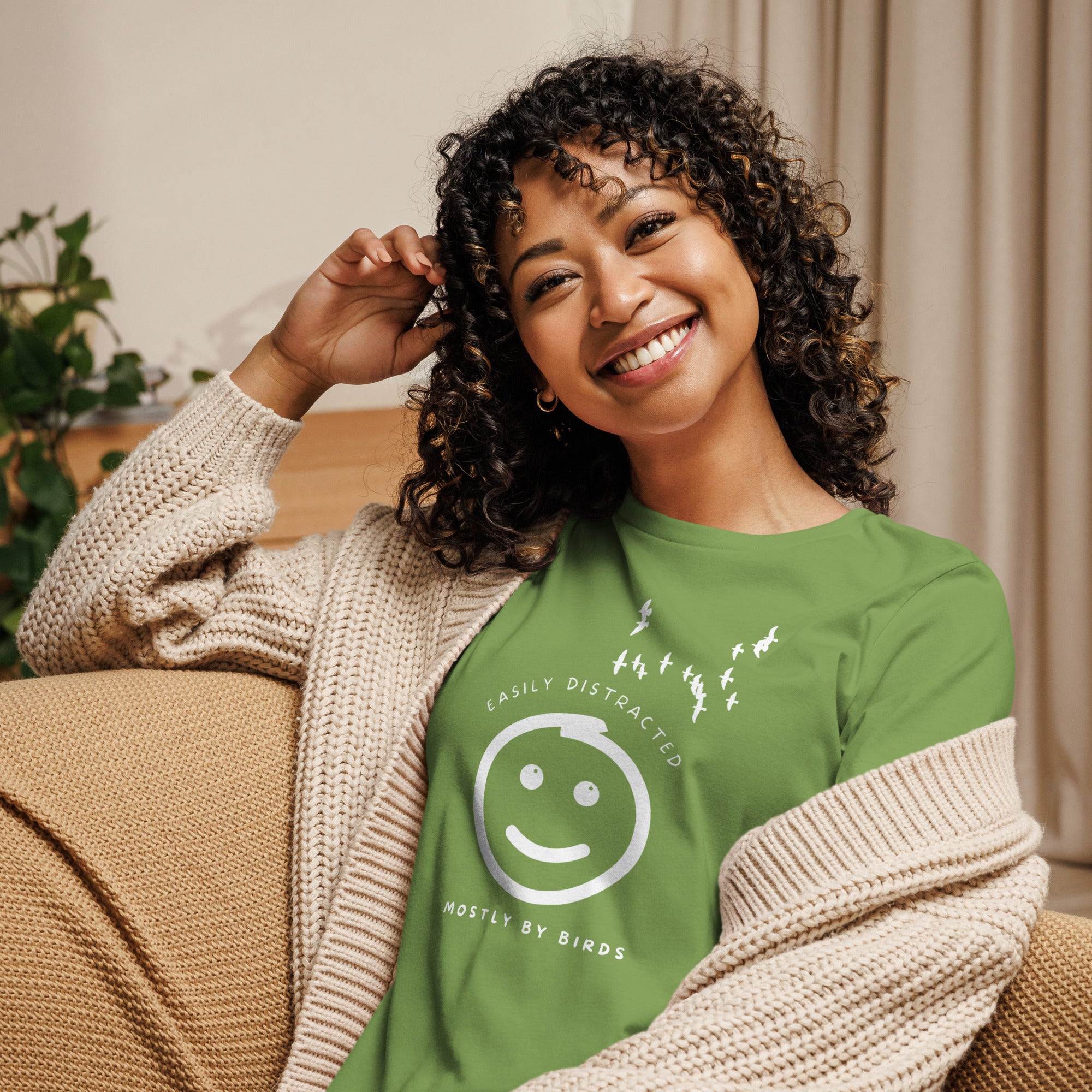 Leaf green women's bird t-shirt with a smiley face looking up and to the side at a flock of birds surrounded by the words, "Easily Distracted" above and, "Mostly by Birds" below. Worn by a woman.