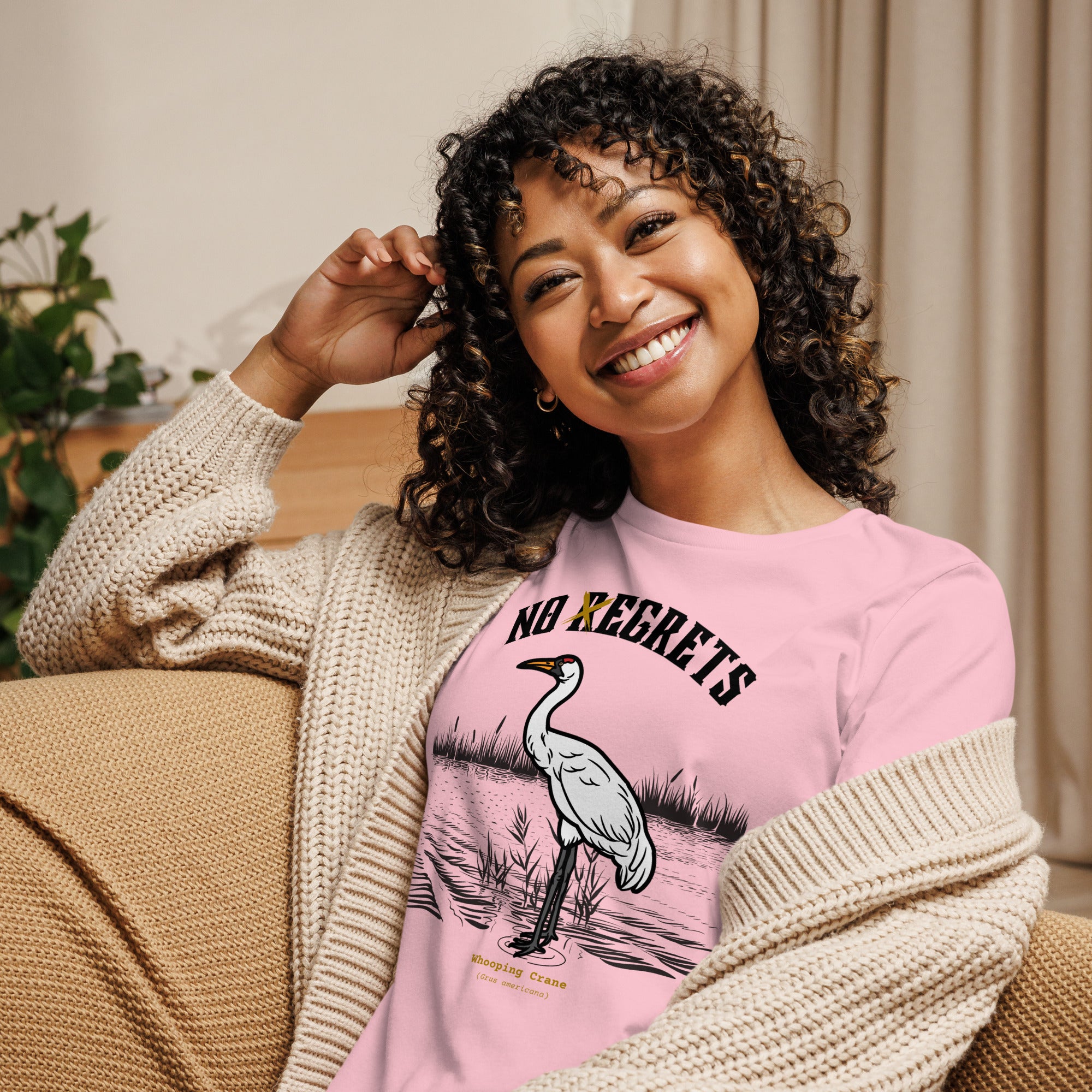 Pink women's bird shirt featuring a play on the "No Regrets" tattoo that has the "R" crossed out to say "No Egrets" with a Whooping Crane below in a wetland setting. Worn by a woman.