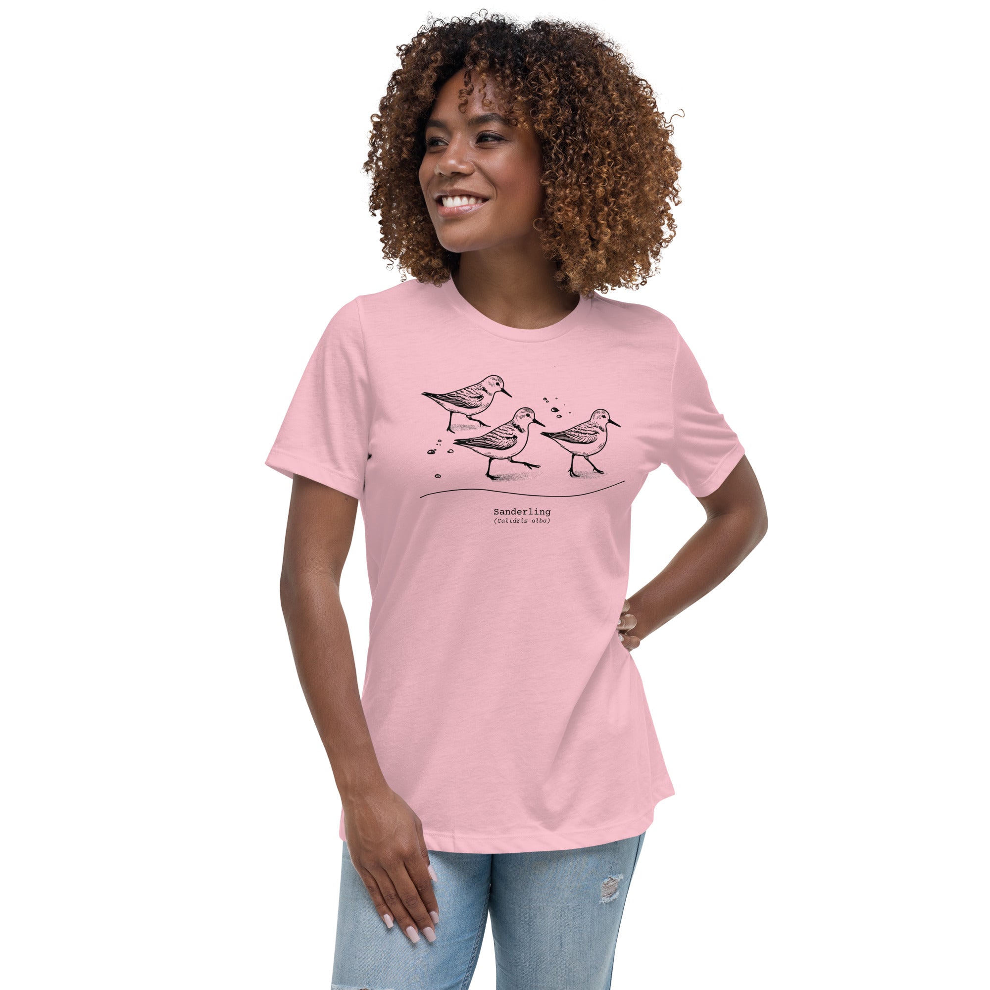 Light pink bird shirt featuring an illustration of a three sanderlings on a beach and the common and scientific names for the bird underneath. Worn by a woman.