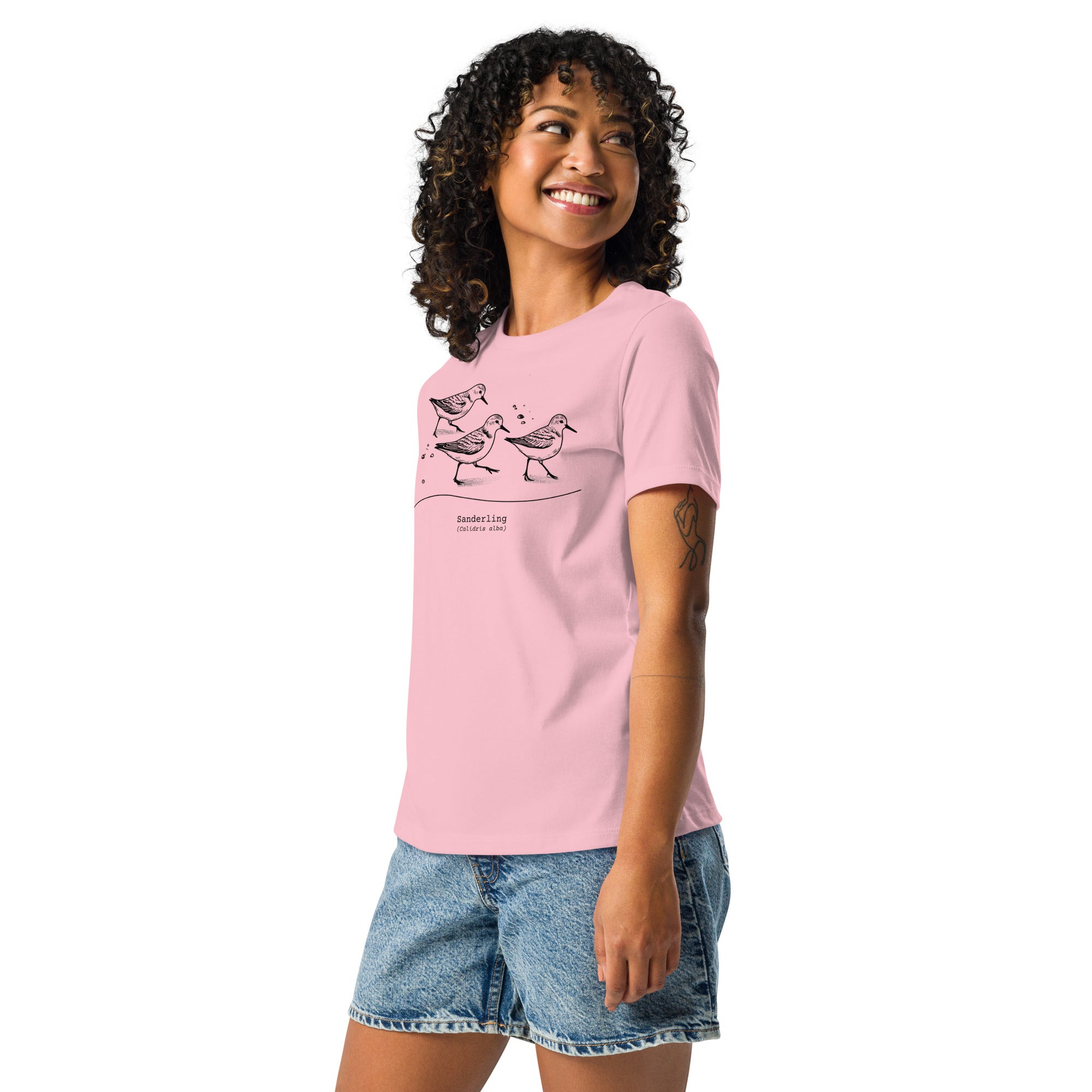 Pink bird shirt featuring an illustration of a three sanderlings on a beach and the common and scientific names for the bird underneath. Worn by a woman.