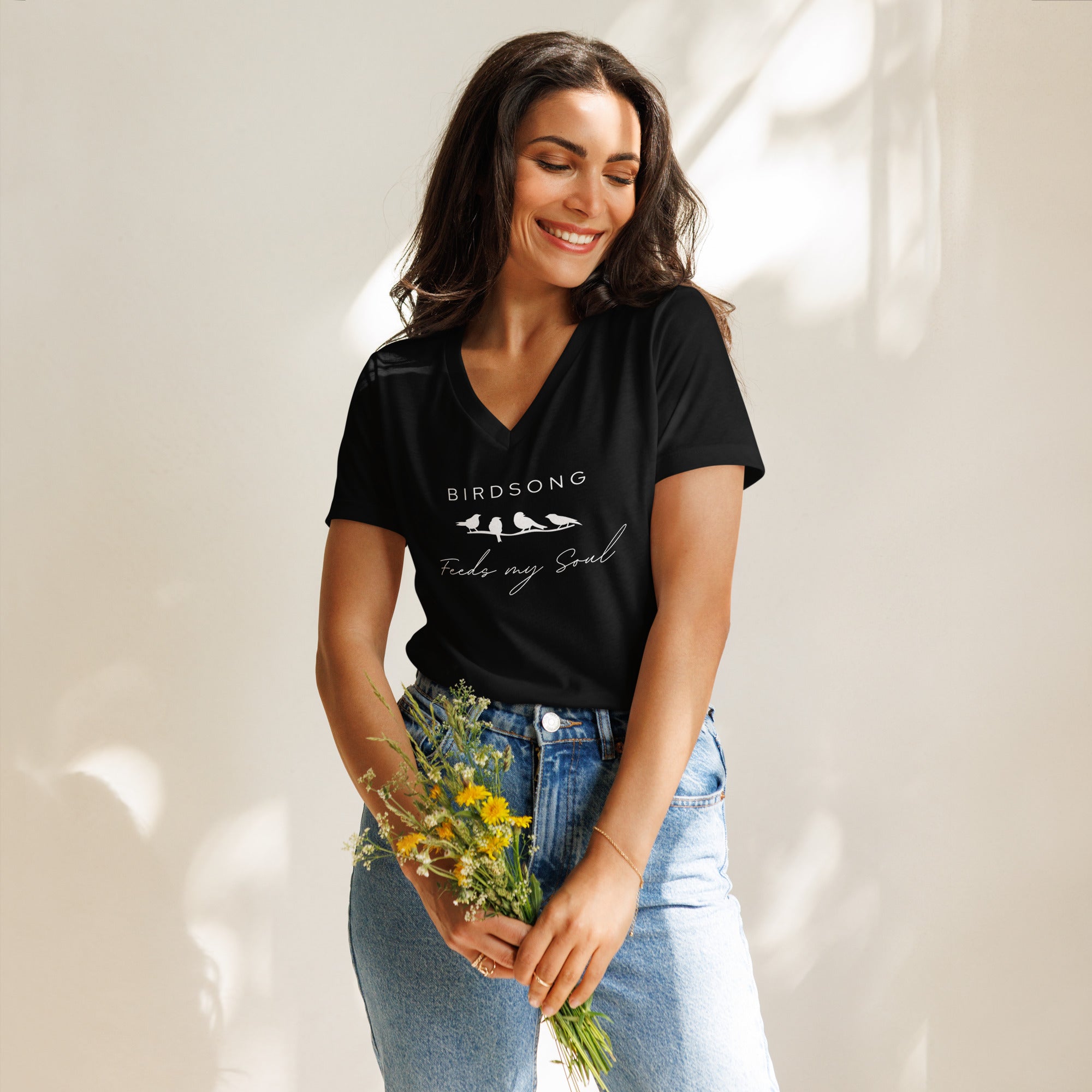 Black women's v-neck bird t-shirt with the words Birdsong feeds my soul placed above and below a white graphic of 4 birds on a branch. Worn by a woman.