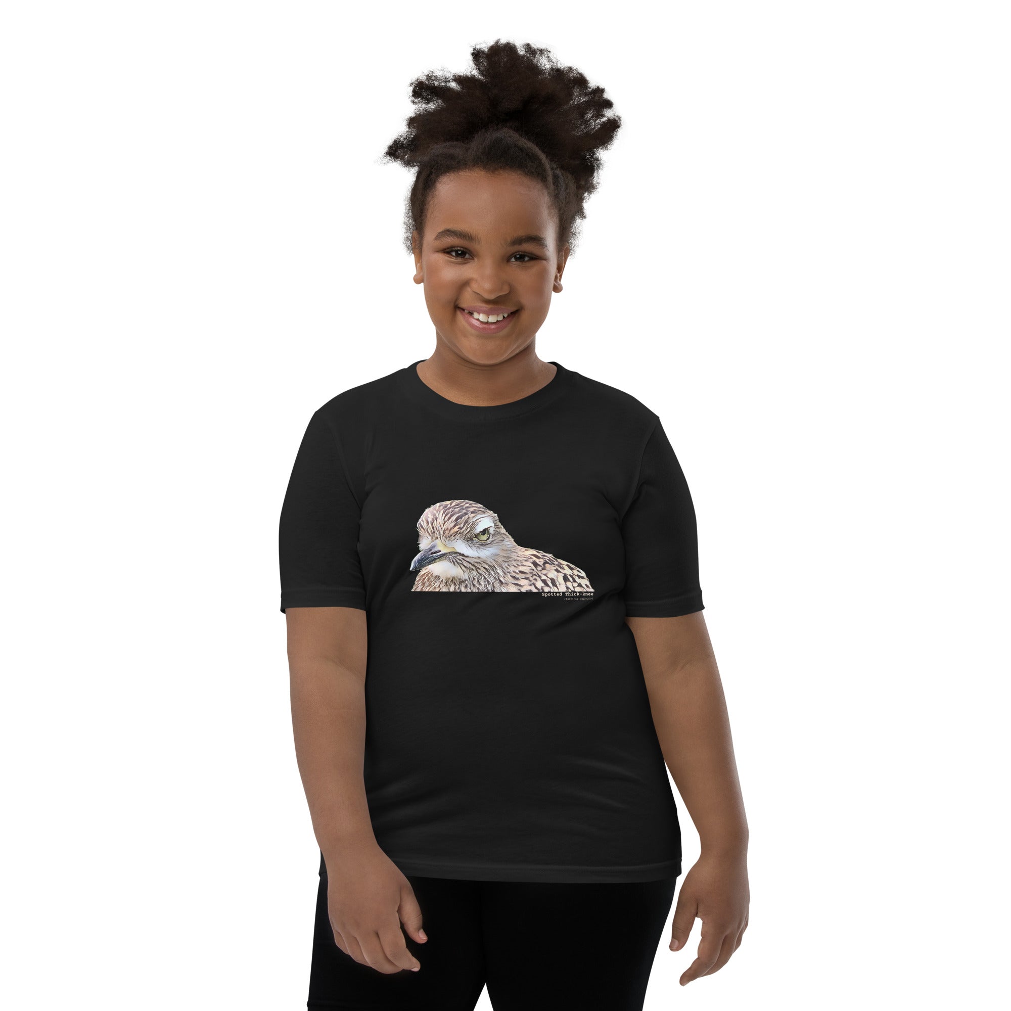 Black unisex youth bird t-shirt with an illustrated picture of a spotted thick-knee bird looking grumpy. The words spotted thick-knee are written below the illustration, including the scientific name.