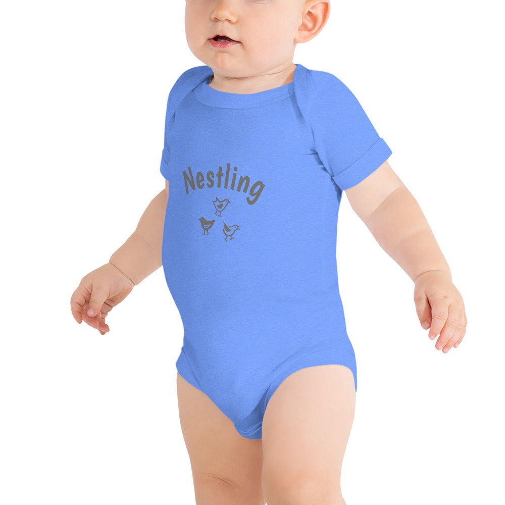 Heather blue one-piece baby suit with the word Nestling on the front above three small birds in a dark grey. Worn by standing baby.